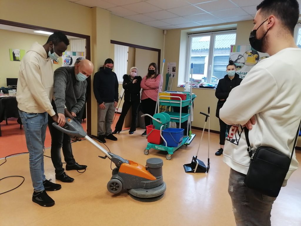 Démonstration d'une autolaveuse devant un groupe de stagiaires masqués, à côté d'un chariot de ménage.