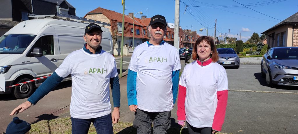 Trois personnes en tee-shirt APAJH Nord posent dans une rue, devant le minibus de l'association.