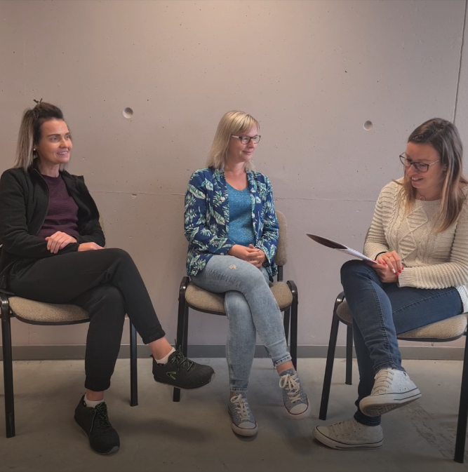 Trois femmes assises sur des chaises échangent, l’une d’elles tenant une feuille à la main