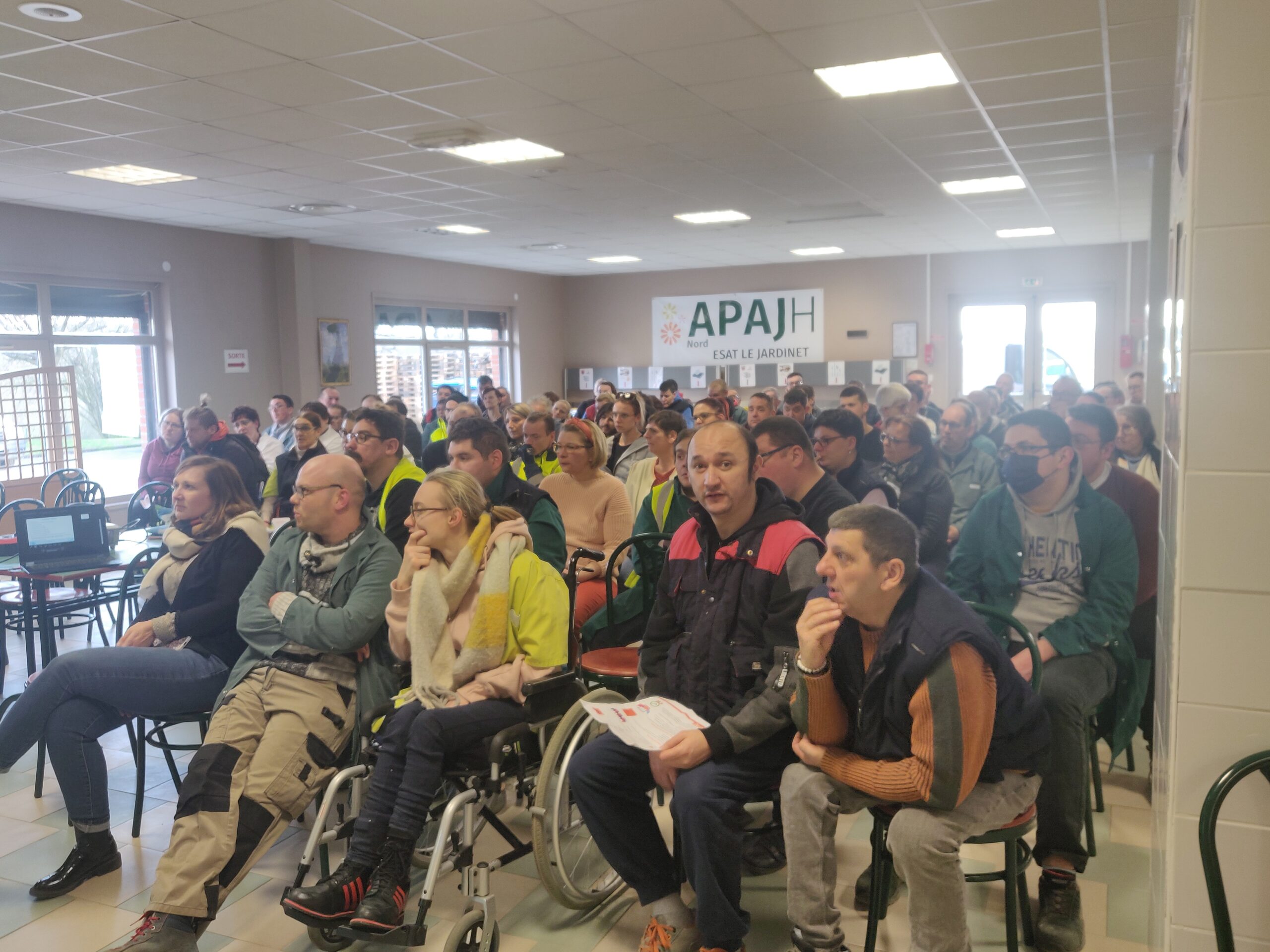 Une salle comble écoute la présentation, sous la banderole de l’ESAT Le Jardinet