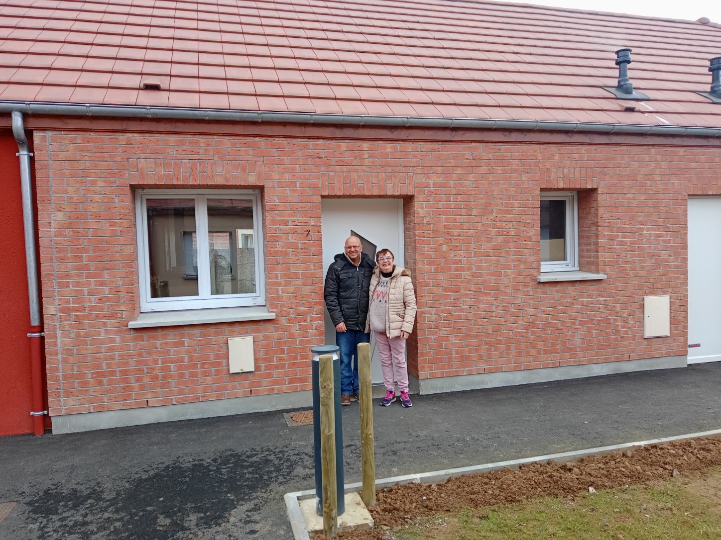 Un homme et une femme posent devant la porte d'entrée d'un pavillon neuf en brique rouge