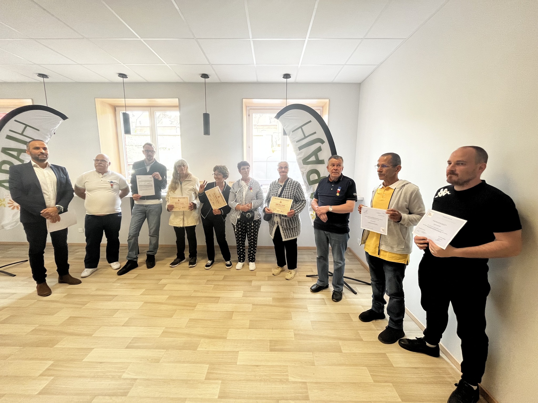 Une dizaine de personnes alignées dans une salle présentent leur diplôme devant deux oriflammes APAJH