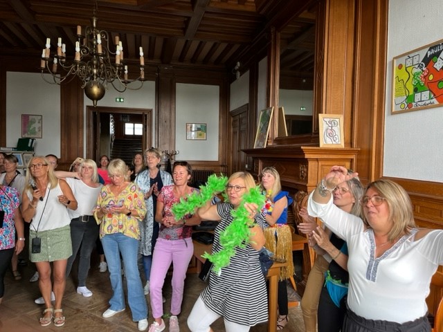 Un groupe de professionnelles applaudit dans une salle lambrissée, l'une porte un boa vert