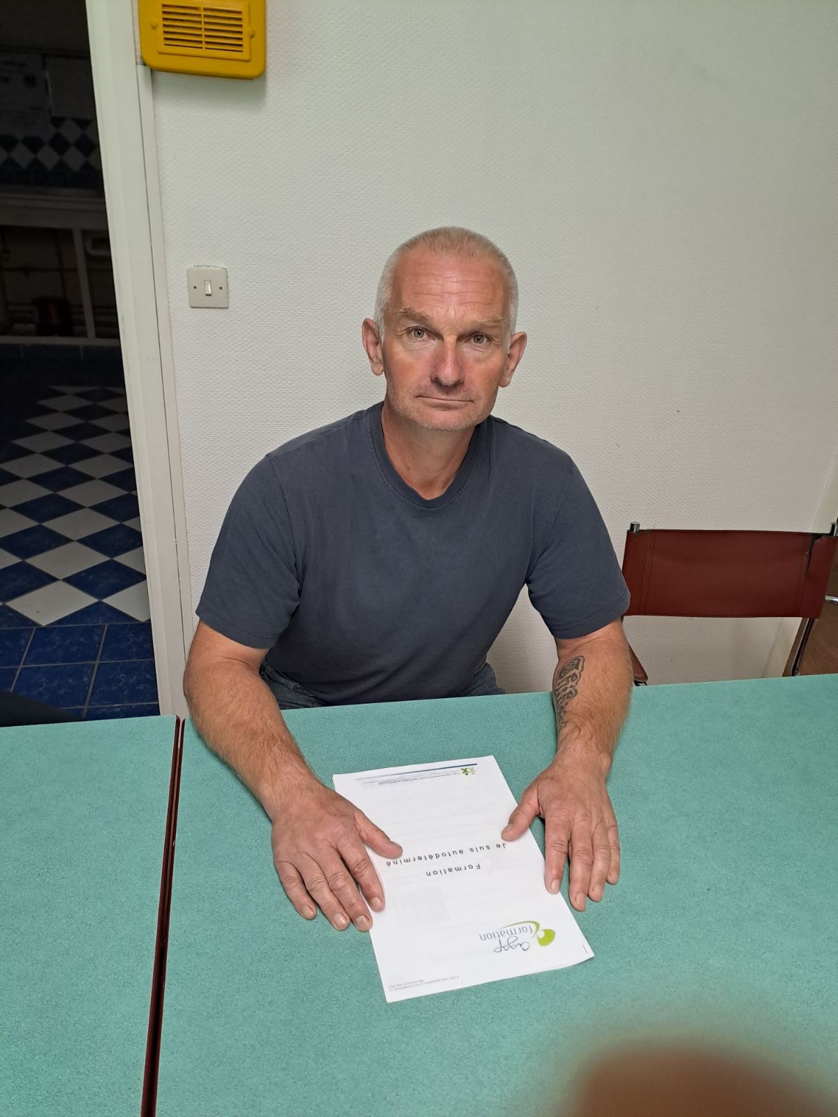 Un homme assis à une table pose les mains sur le livret de la formation « Je suis autodéterminé ».
