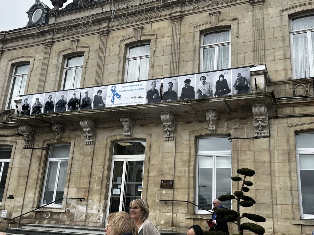 Façade d'un hôtel de ville portant une frise de portraits en noir et blanc et le panneau « Journée mondiale de sensibilisation à l'autisme, 2 avril 2024 ».