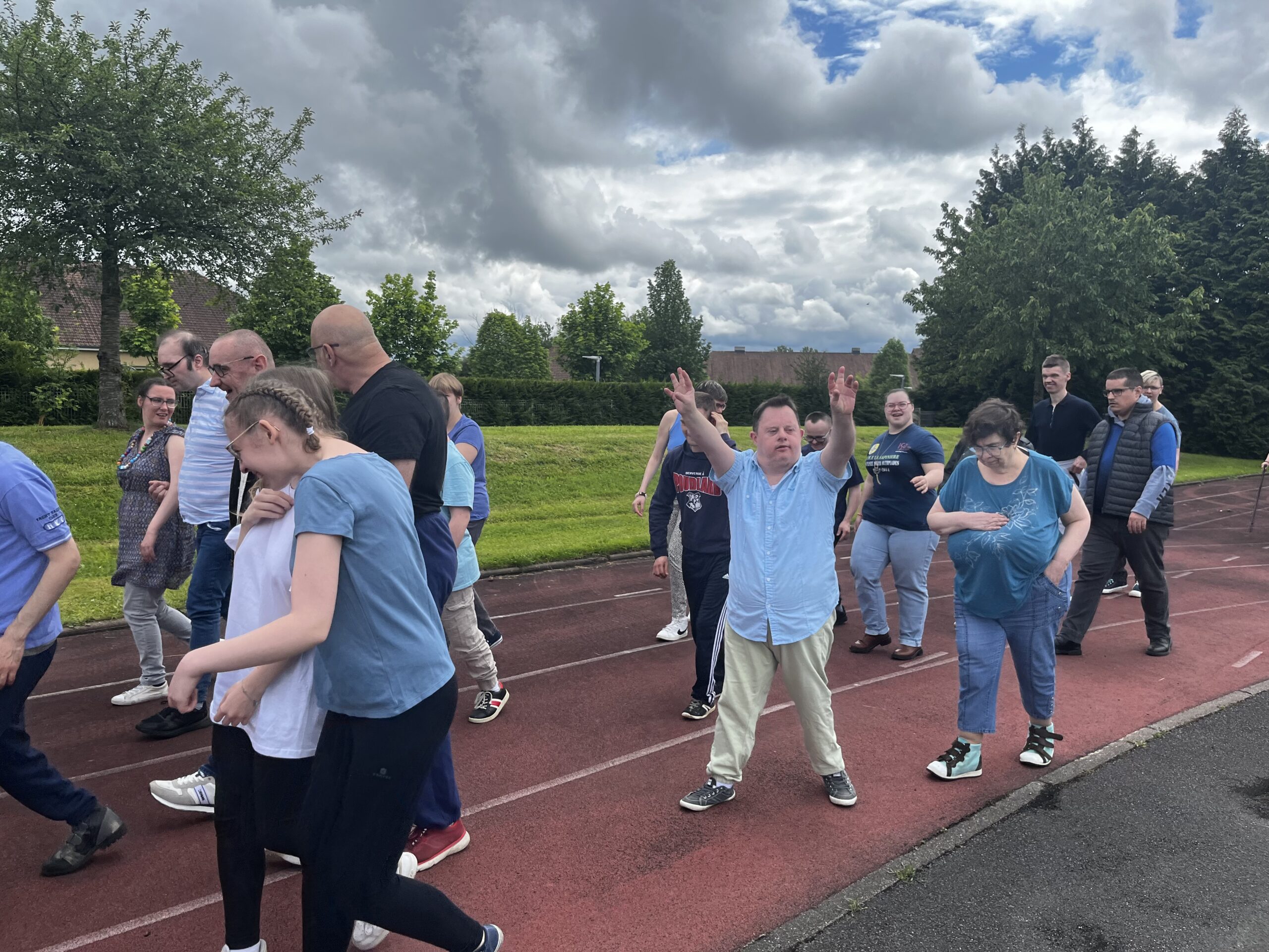 Un groupe marche sur une piste d'athlétisme, un participant lève les bras, sous un ciel nuageux.