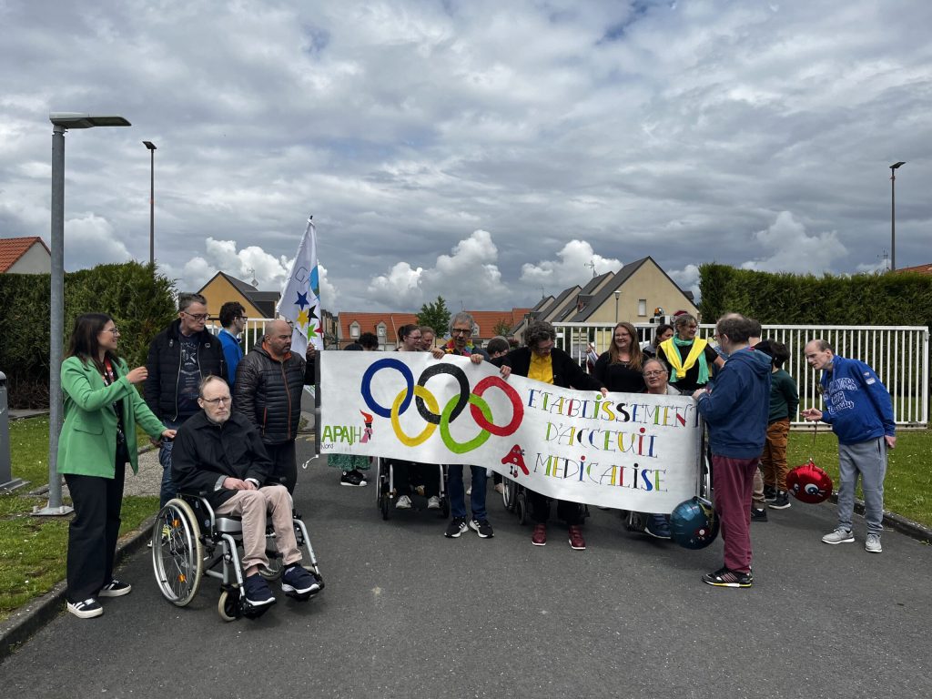 Groupe réuni derrière une banderole peinte « Établissement d'accueil médicalisé » ornée des anneaux olympiques.