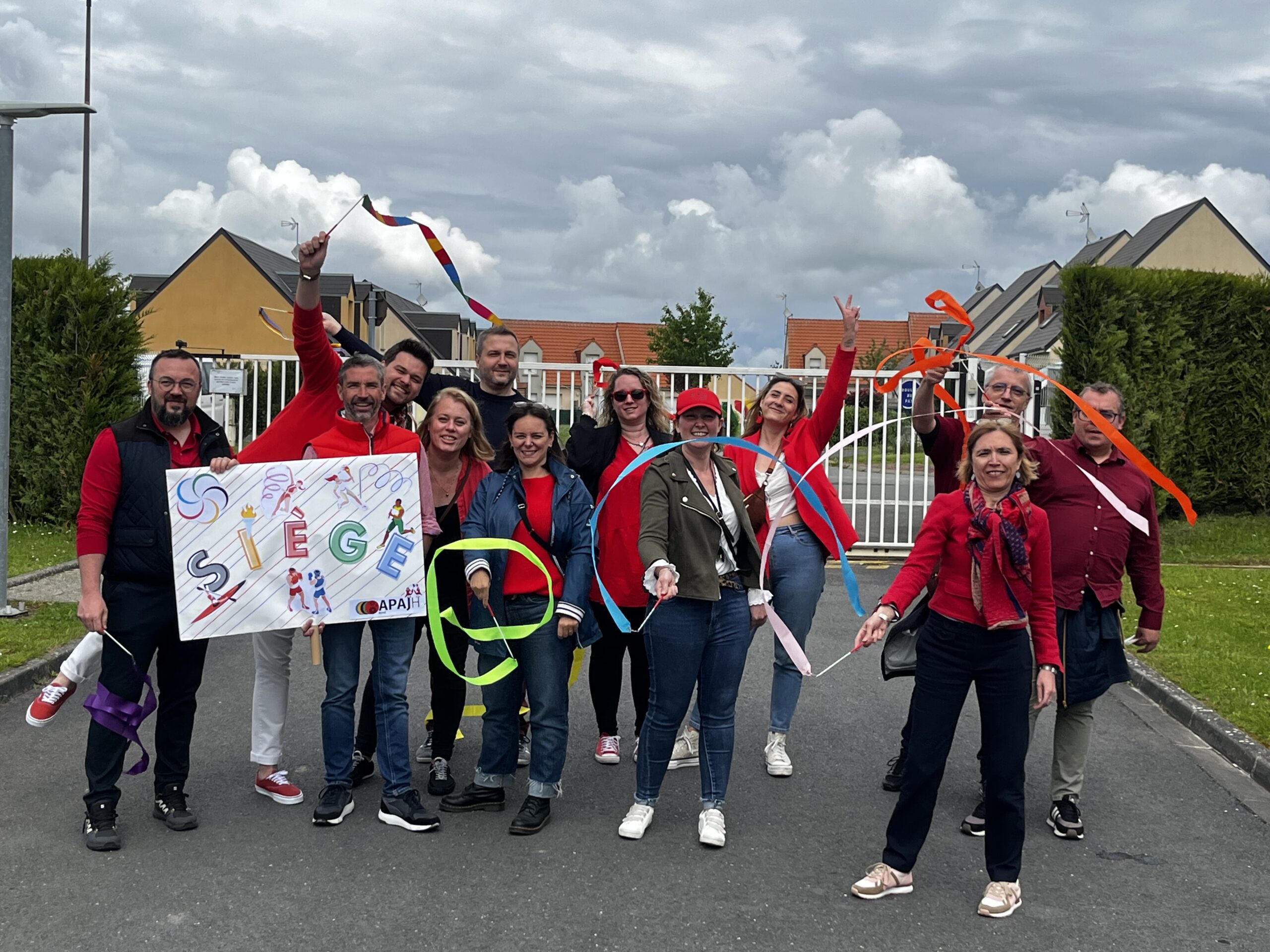 Une équipe en tenue rouge brandit des rubans et une pancarte « Siège » ornée d'anneaux olympiques, dans la rue.
