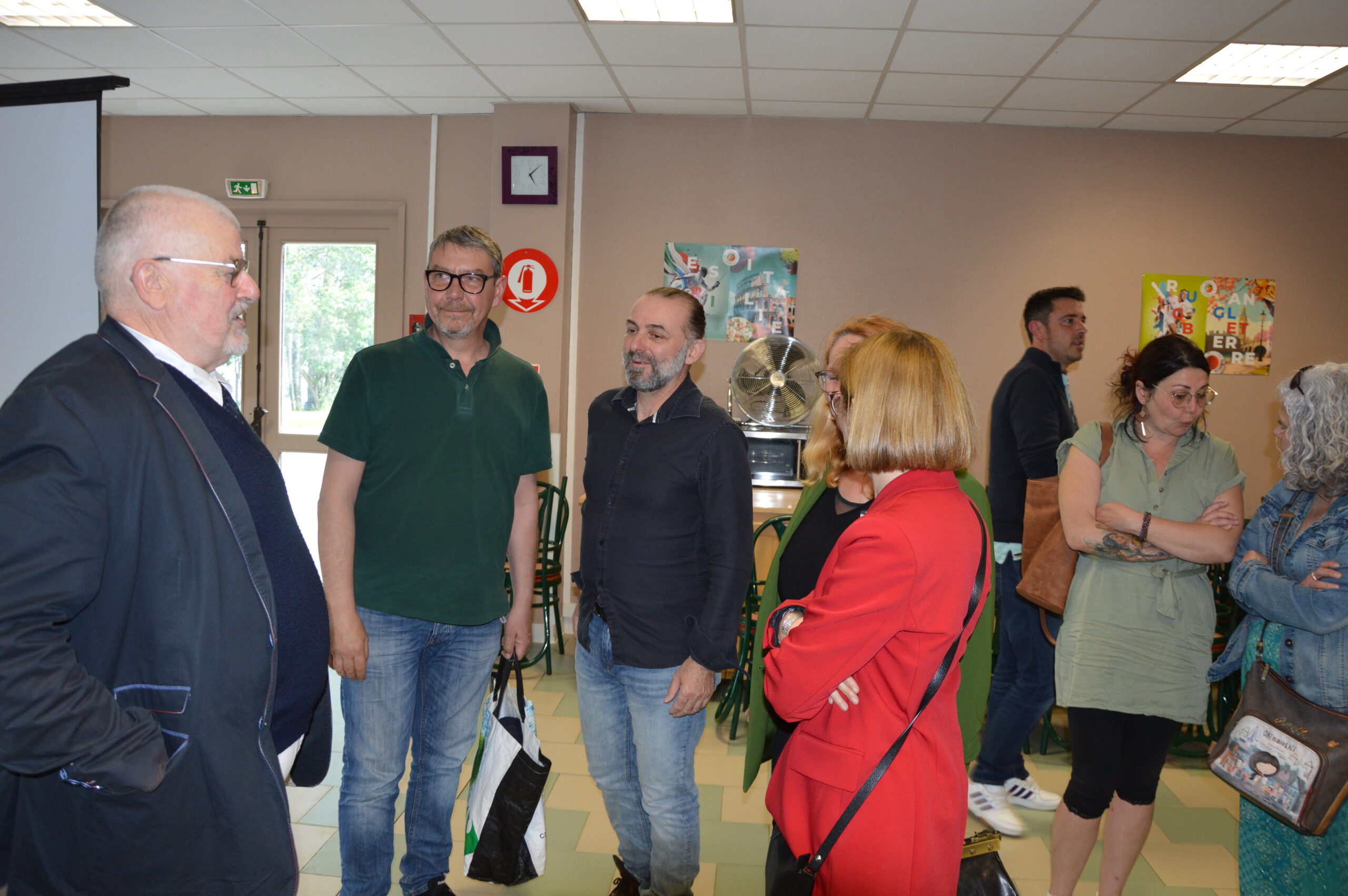 Plusieurs adultes debout dans une salle d'activité, discutant par petits groupes.