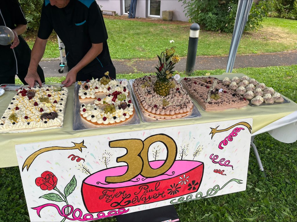 Buffet dressé en extérieur pour les 30 ans du foyer Paul Levayer : grands gâteaux et affiche peinte « 30 ».
