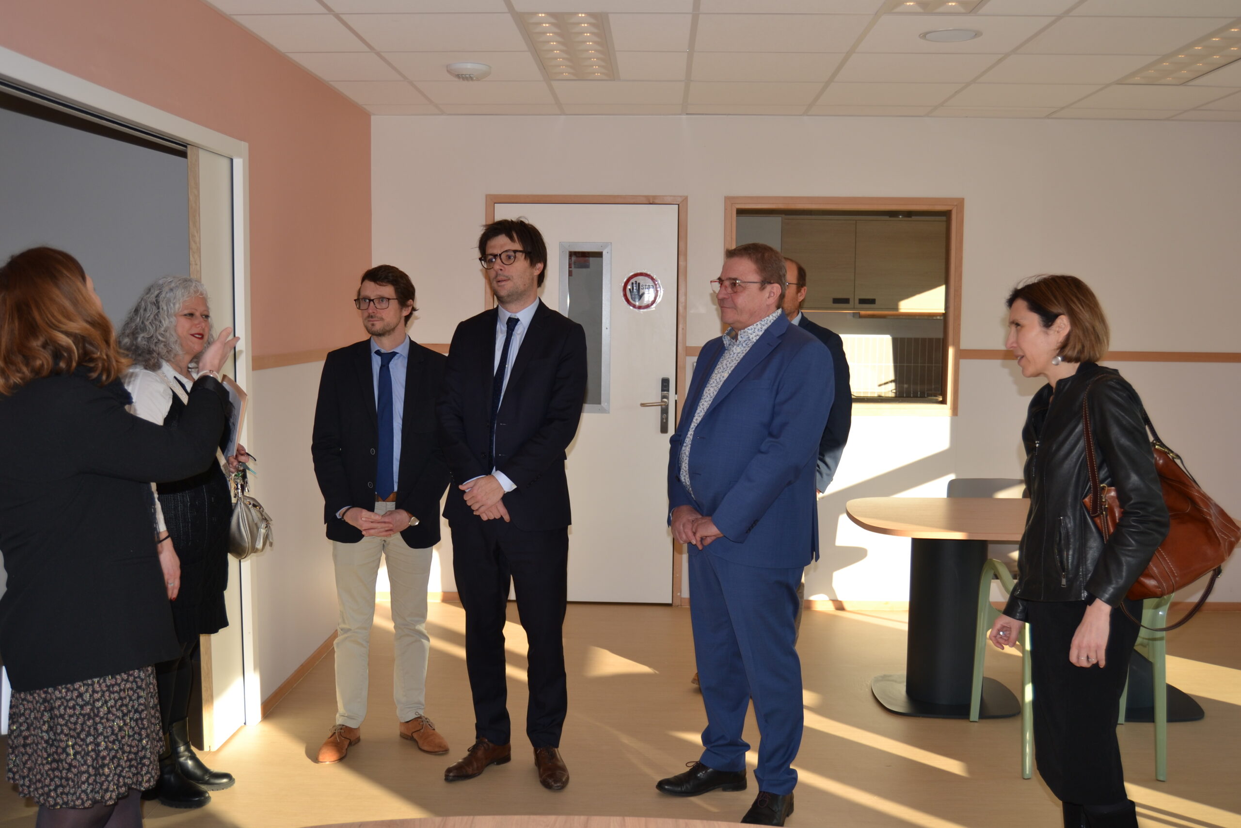 Visite de locaux neufs : une femme présente une pièce à un petit groupe en tenue de ville.
