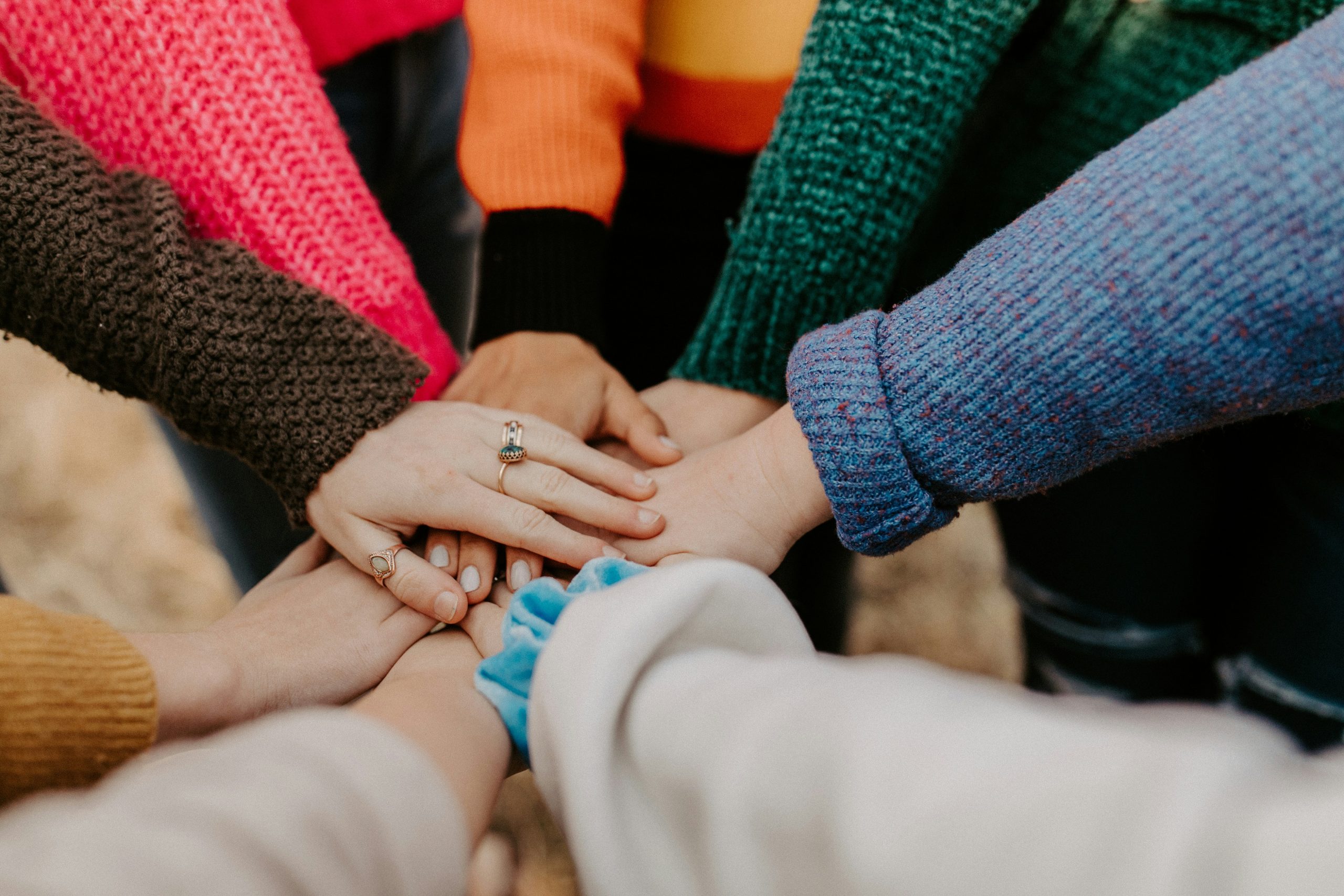 Plusieurs personnes en pull coloré posent leurs mains les unes sur les autres en signe d'équipe