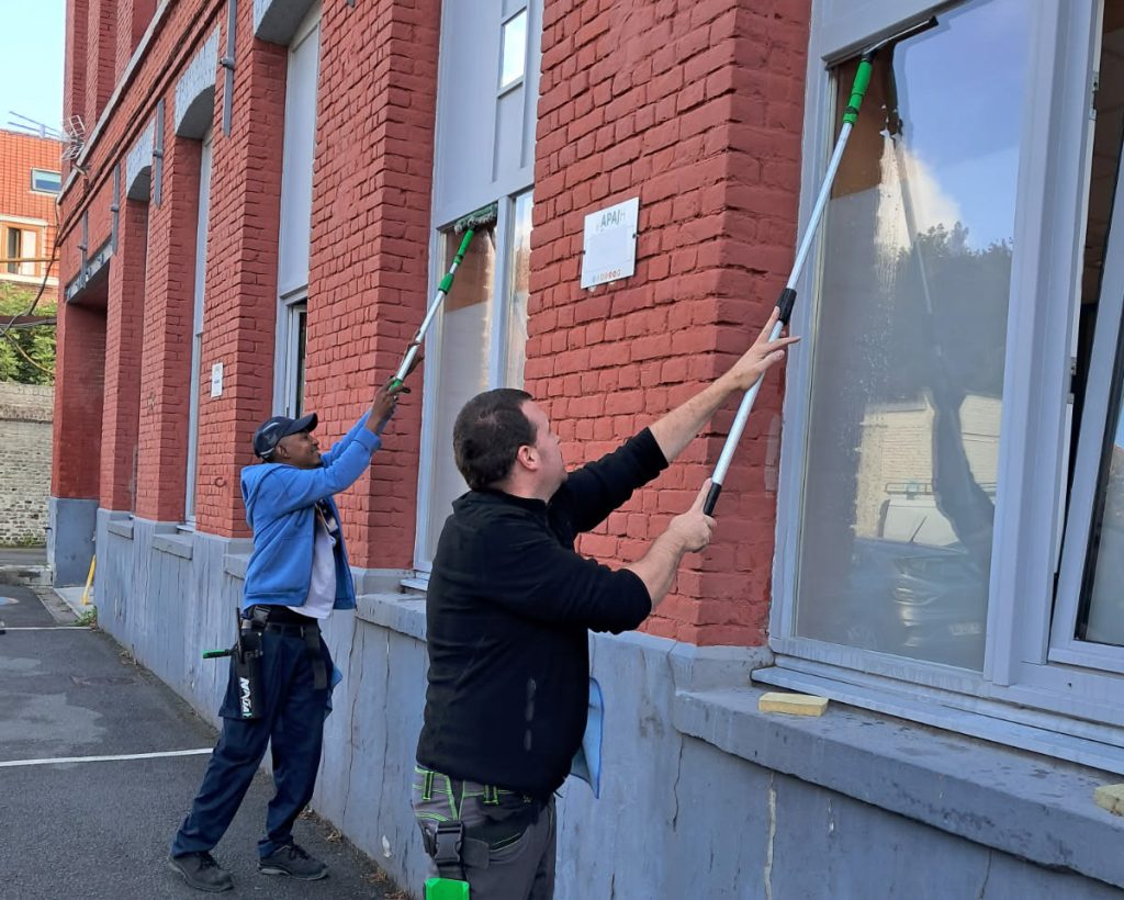 Deux agents du Sextant lavant les vitres d’un bâtiment en brique à la perche télescopique