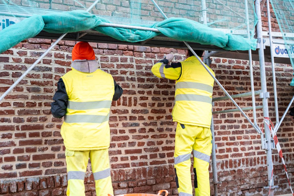 Deux ouvriers en tenue haute visibilité rejointoyant un mur en brique sous échafaudage
