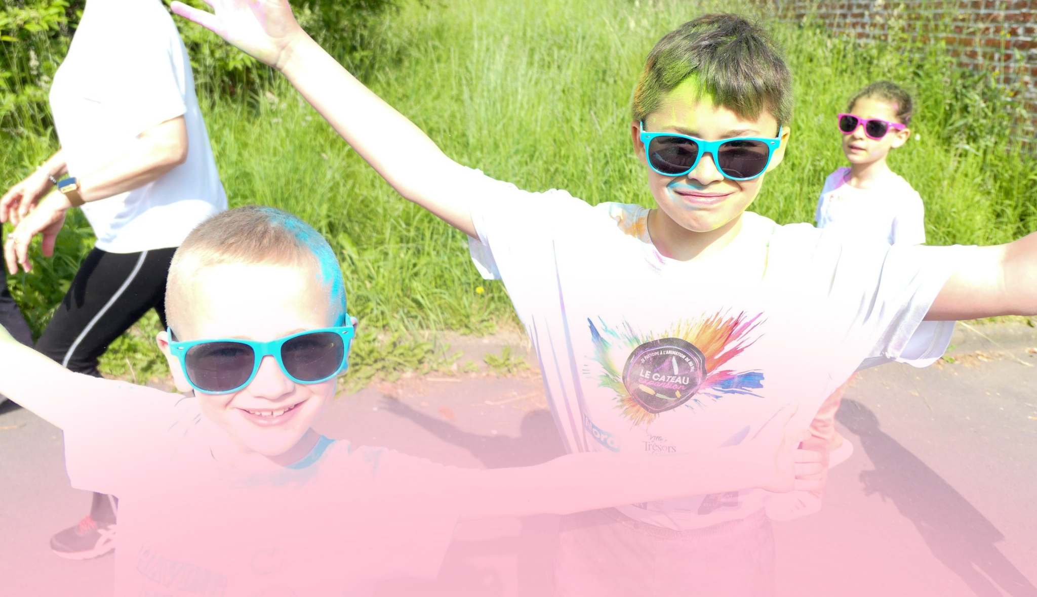 Deux enfants en lunettes de soleil, cheveux et tee-shirts poudrés de couleurs, bras écartés pendant une course colorée.