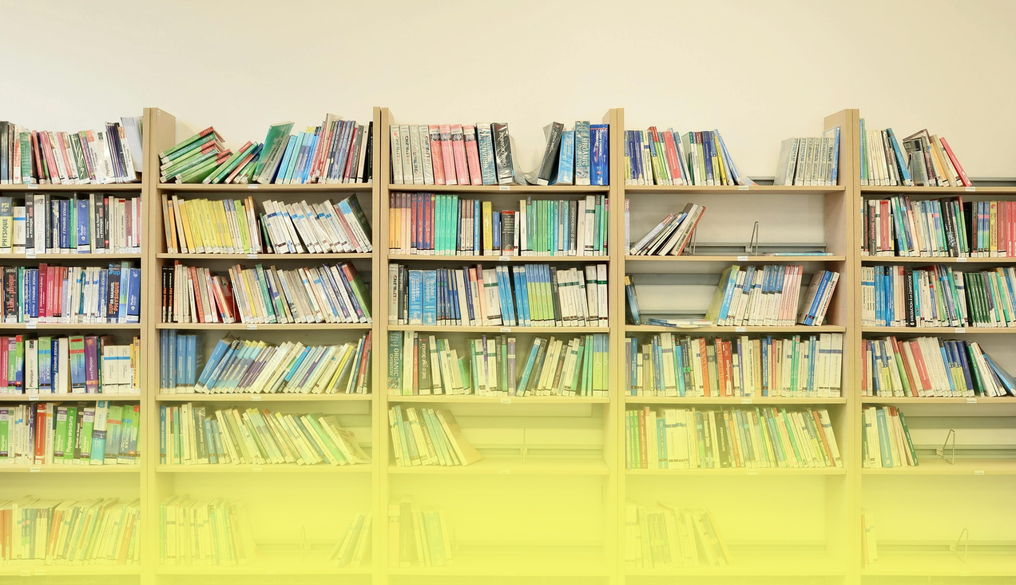 Rayonnages d'une bibliothèque remplis de manuels et d'ouvrages scientifiques, sur plusieurs étagères de bois clair.