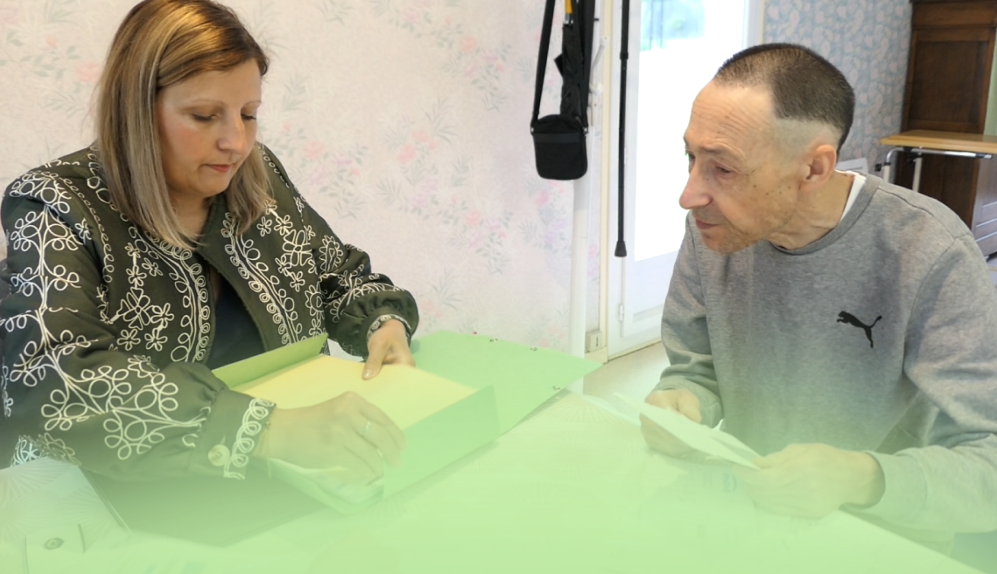 Une femme et un homme assis à une table examinent ensemble des dossiers papier, dans un logement.