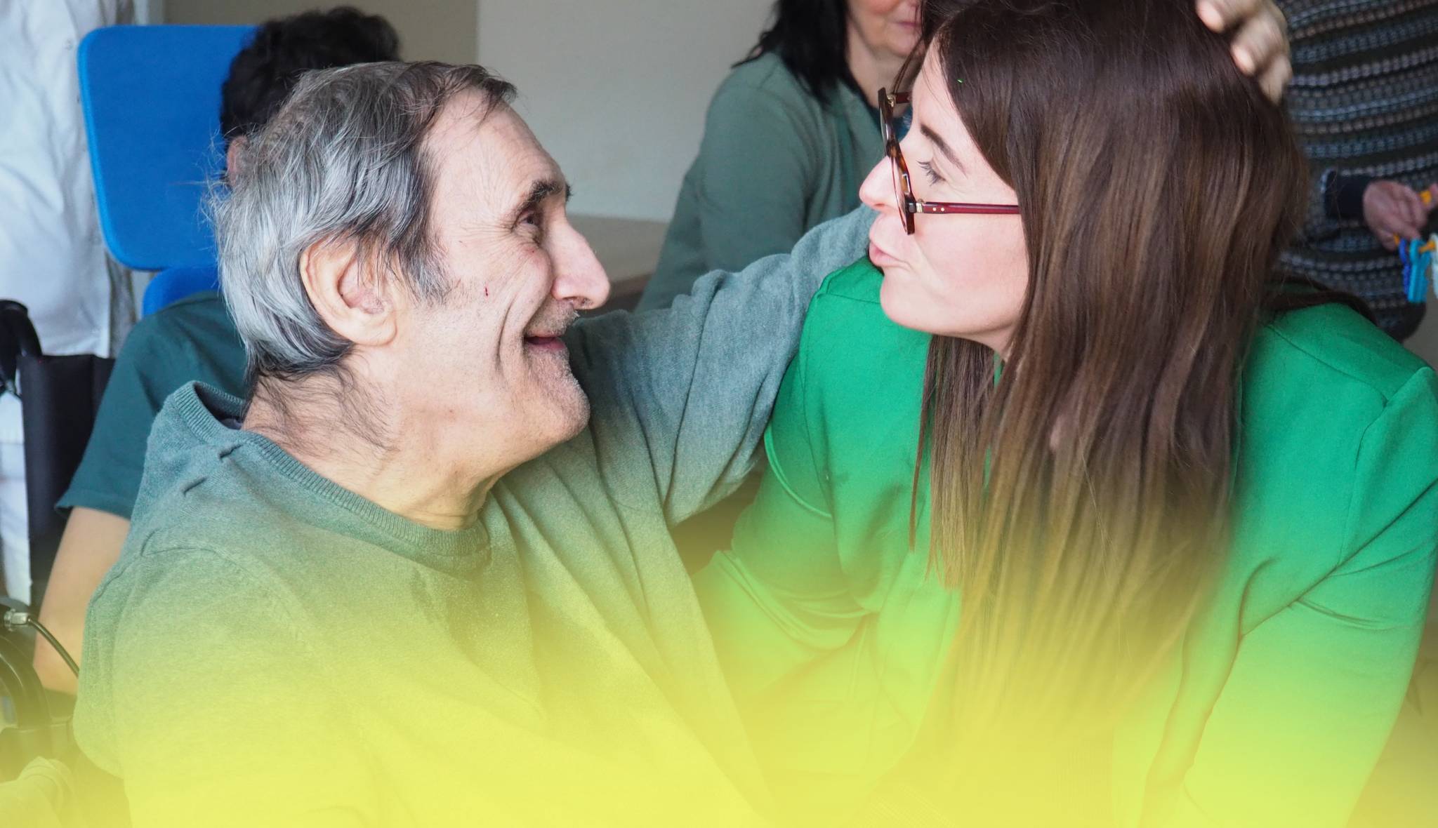 Un homme âgé et une jeune femme, bras sur l'épaule l'un de l'autre, se regardent en souriant.